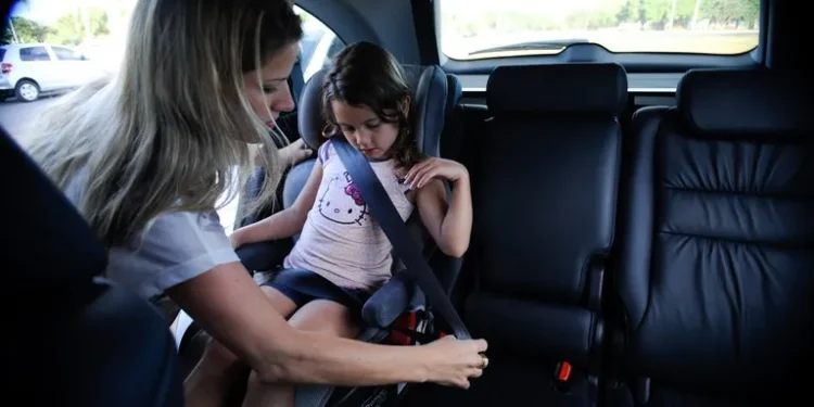 Mãe ajustando o cinto de segurança em uma criança na cadeirinha de carro.