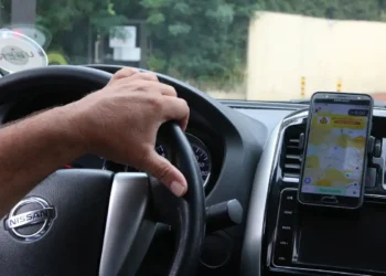 Motorista dirigindo veículo com aplicativo de transporte aberto no celular.