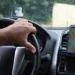Motorista dirigindo veículo com aplicativo de transporte aberto no celular.