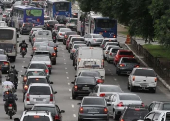 Trânsito congestionado em uma avenida, com carros e ônibus parados na via.