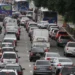 Trânsito congestionado em uma avenida, com carros e ônibus parados na via.