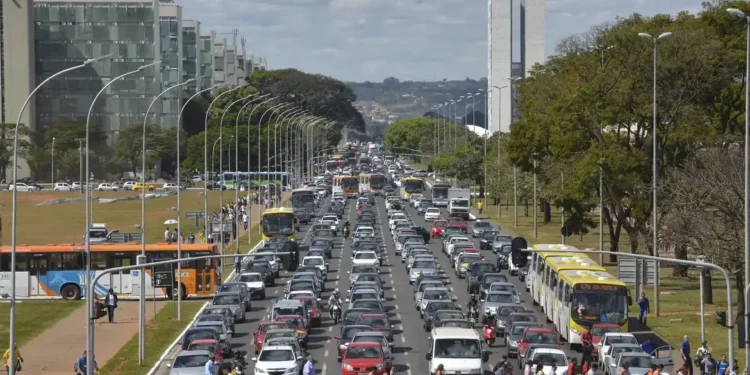 Trânsito intenso com veículos e pedestres se cruzando em grande avenida.