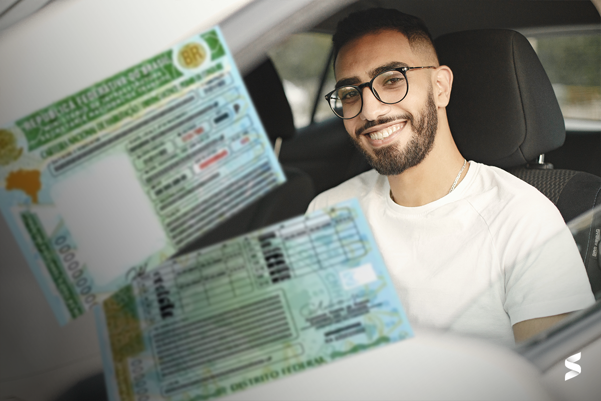 Homem sorridente segurando a Carteira Nacional de Habilitação dentro do carro