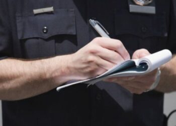 Policial registrando notificação de infração de trânsito em bloco de papel.