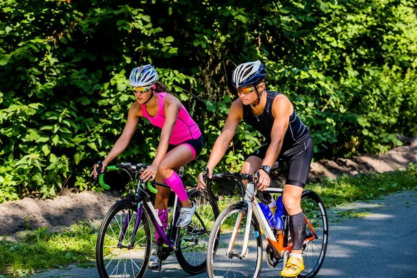 Duas ciclistas femininas pedalando em ciclovia rodeada por área verde