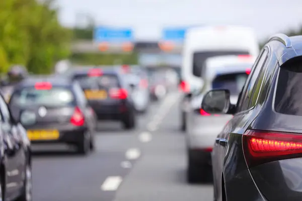 Carros em congestionamento na estrada, com tráfego lento e sinais de trânsito visíveis.