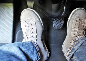 Pés usando tênis acionando o pedal da embreagem em carro com câmbio manual