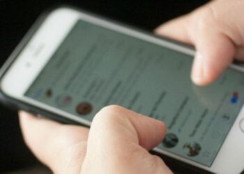 Pessoa segurando um smartphone com a tela mostrando mensagens de redes sociais, representando alerta sobre golpes online de CNH gratuita.