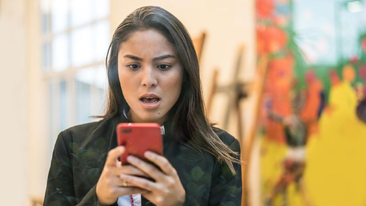 Mulher com expressão preocupada olhando para o celular, simbolizando receio diante de possíveis golpes nas redes sociais.