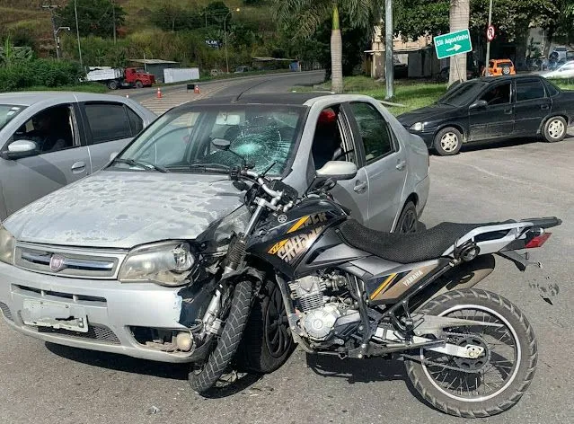 Moto preta encostada na frente de carro prata com para-brisa quebrado após colisão