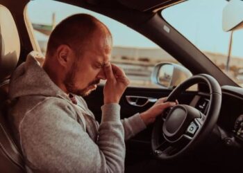 Jovem motorista com olhos fechados, lutando contra o sono durante a direção