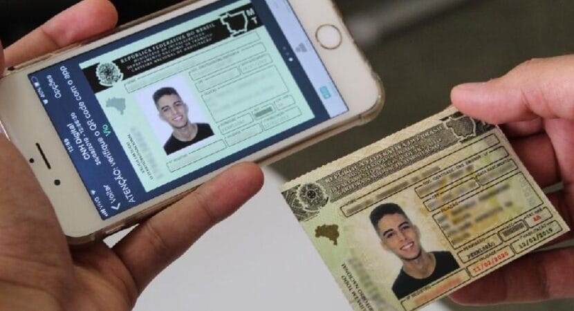 Imagem de uma pessoa segurando o smartphone com a versão digital da CNH e a versão física da carteira de habilitação.
