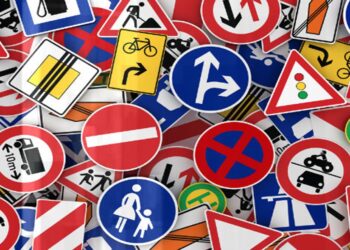 Conjunto colorido de placas de sinalização de trânsito variadas, incluindo sinais de proibição, alerta e orientação, com símbolos diversos.