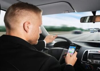 Distração ao Dirigir: Motorista olhando o celular enquanto dirige em rodovia movimentada