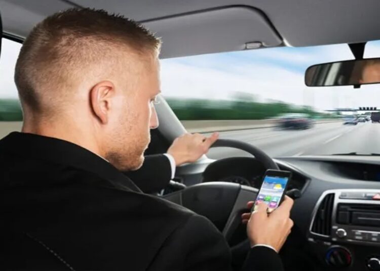 Distração ao Dirigir: Motorista olhando o celular enquanto dirige em rodovia movimentada