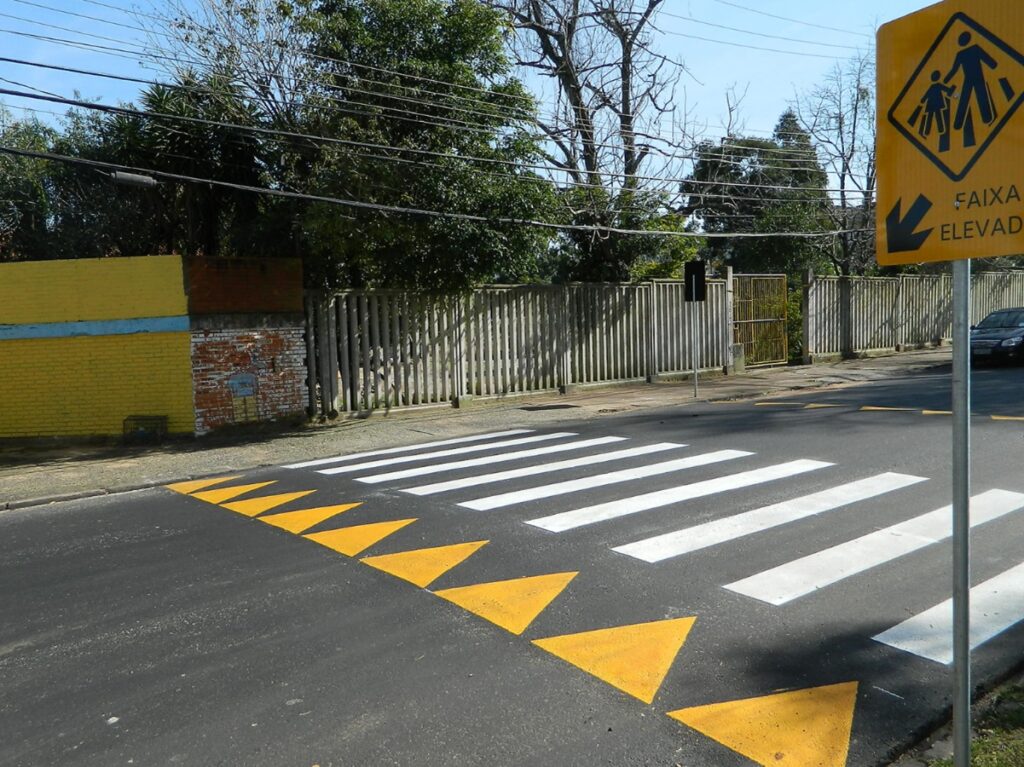 Faixa de pedestre elevada com sinalização de travessia na calçada e placas indicativas.