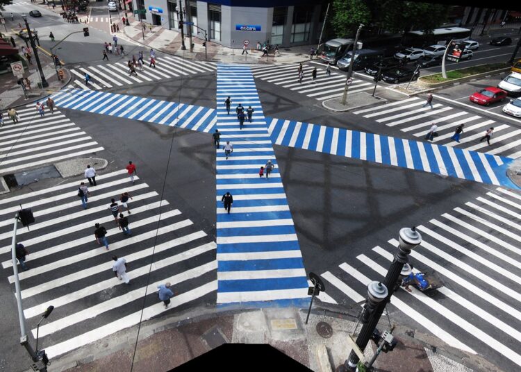 Cruzamento com faixas de pedestre em padrão X, em área urbana.