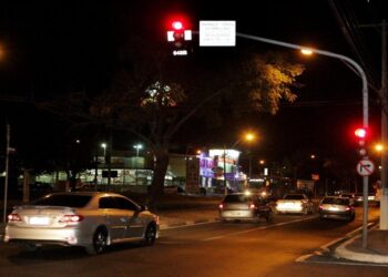 Carros parados em cruzamento com sinal vermelho durante a noite em área urbana.