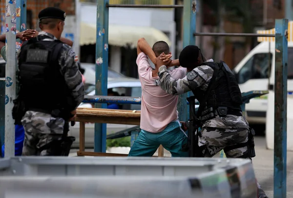 Detenção de indivíduo por policiais em área urbana, com duas forças de segurança atuando para conter o suspeito.