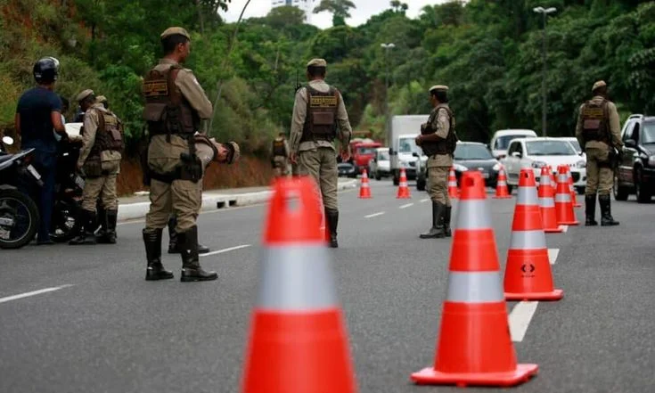 Agentes de trânsito durante uma blitz, com cones de sinalização organizando o tráfego em uma estrada movimentada.