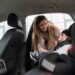 Mãe ajustando cadeirinha de criança pequena no banco traseiro do carro