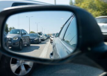 Imagem mostrando o reflexo de um engarrafamento no retrovisor de um carro, com veículos parados em uma estrada. Lei do retrovisor.