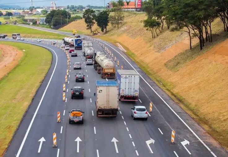 Rodovia com várias faixas em obra, veículos circulando com cones de sinalização delimitando as faixas.