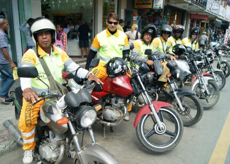 Mototaxistas em suas motos, com uniformes amarelos e capacetes, aguardando clientes