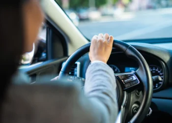 Mão de empresária segurando o volante de um carro, conduzindo com atenção na cidade