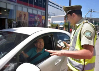 Policial realizando teste de bafômetro em motorista durante fiscalização de trânsito em um carro oficial."
