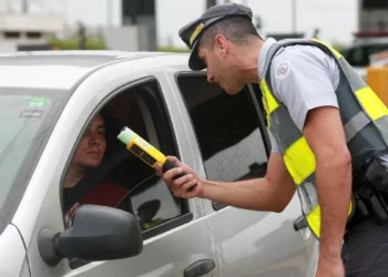 Policial realizando teste de bafômetro em motorista durante blitz de trânsito.