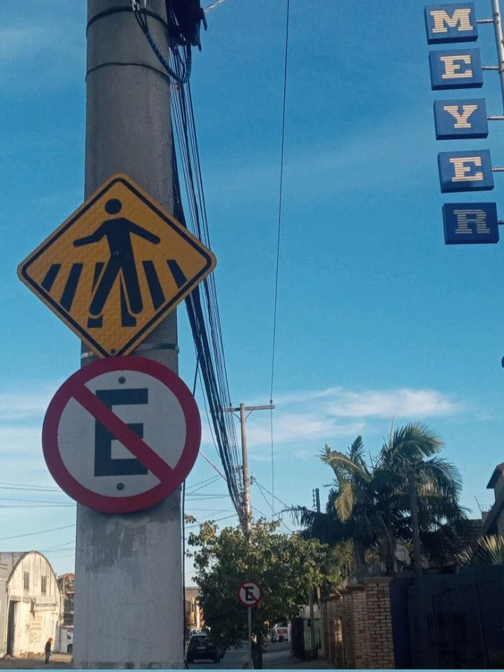 Placa de 'Proibido Estacionar' e sinalização de faixa de pedestre, destacando infrações de estacionamento irregular