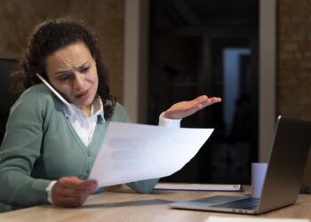 Mulher olhando documento enquanto fala ao telefone, simbolizando a distração comum de motoristas ao dirigir e não perceber infrações de trânsito.