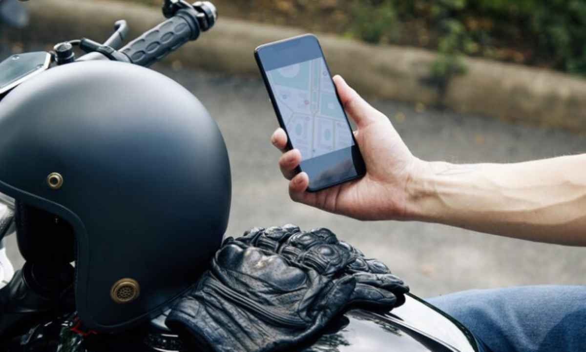 Mão de motociclista segurando um celular com aplicativo de navegação.