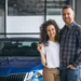 Casal jovem feliz em showroom de carros com chave de carro, aproveitando desconto para MEI em 2025