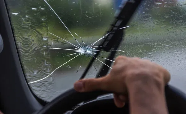 Para-brisa trincado de carro em um dia chuvoso, destacando os riscos de dirigir com vidro danificado.