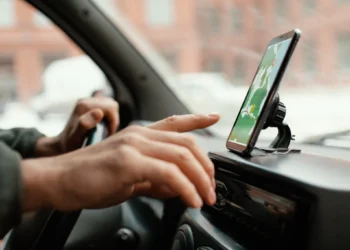 Homem manipulando celular em suporte de carro enquanto dirige, ilustrando as regras de trânsito sobre o uso de dispositivos móveis.