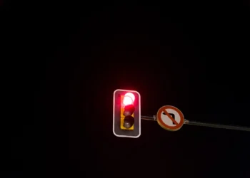 Semáforo vermelho à noite com placa de proibido virar à esquerda