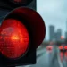 Close no sinal de trânsito vermelho aceso com a estrada molhada e edifícios desfocados ao fundo