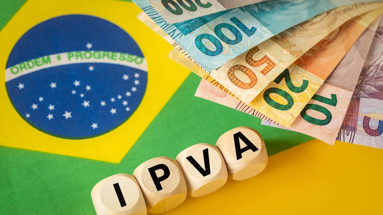 Cubos com letras formando IPVA, notas de real e bandeira do Brasil ao fundo.