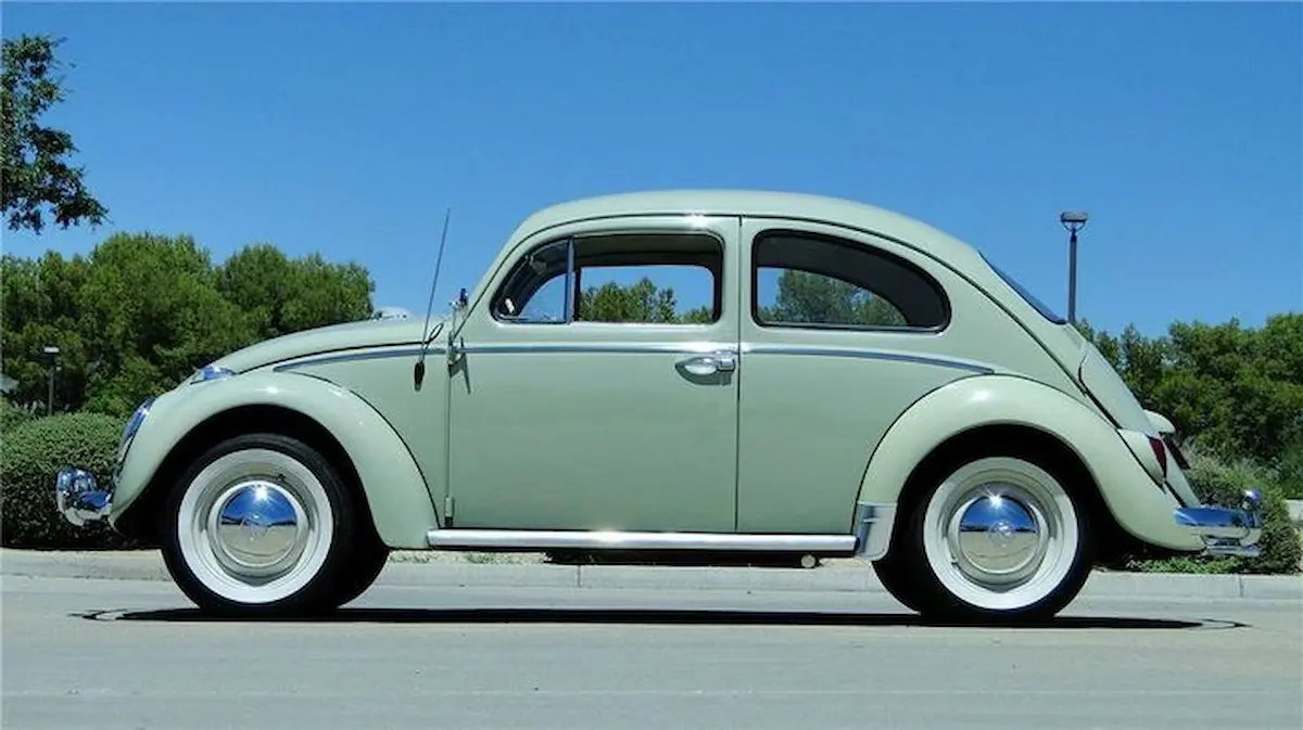 Carro Volkswagen Fusca vintage estacionado em rua com céu azul e vegetação ao fundo.