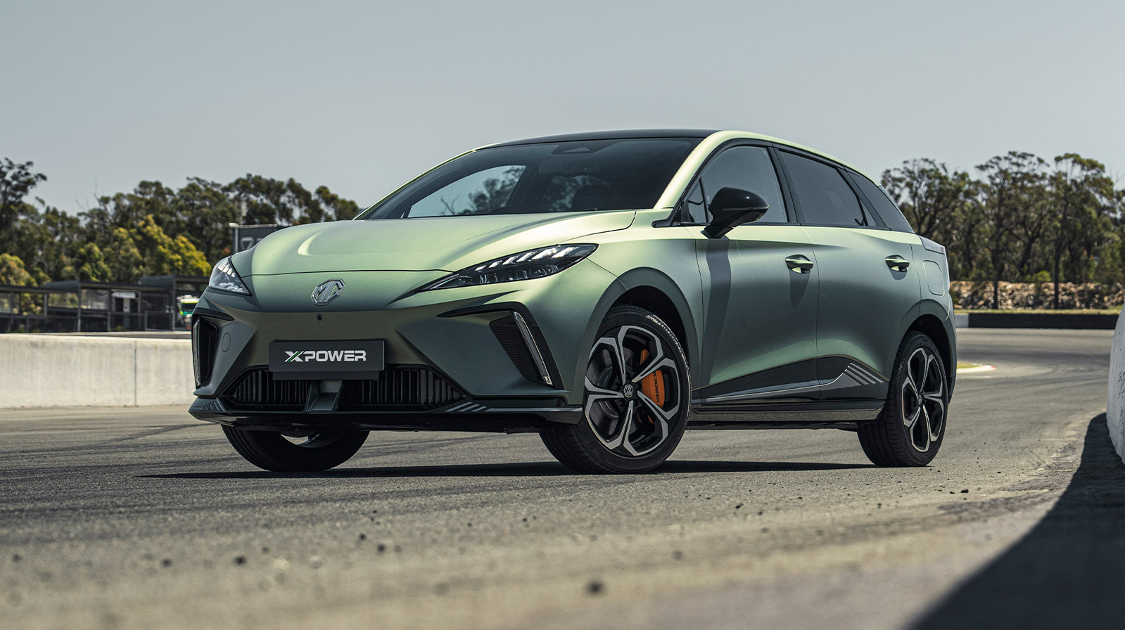 MG4 Comfort verde estacionado em pista de asfalto com árvores ao fundo.