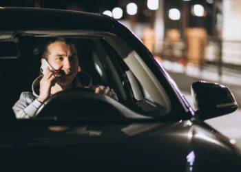 Homem dentro de um carro, sorrindo e falando ao celular, representando uma infração que pode resultar em multa mesmo com o veículo parado.
