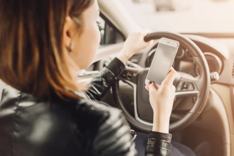 Mulher dirigindo e usando o celular, representando o risco de ser multada mesmo com o carro parado, devido ao uso inadequado do telefone ao volante.