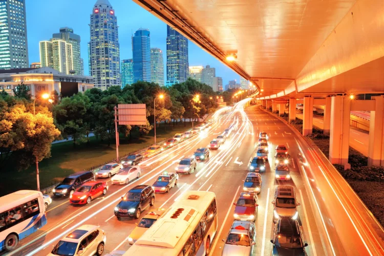 Carros e ônibus parados em congestionamento sob viaduto iluminado ao entardecer na cidade