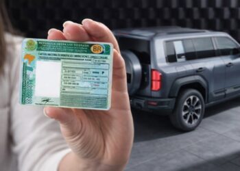 Pessoa segurando CNH brasileira ao lado de SUV elétrico estacionado em ambiente moderno