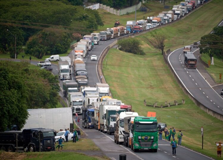 Filas de caminhões parados ocupam pista de rodovia com motoristas ao lado dos veículos