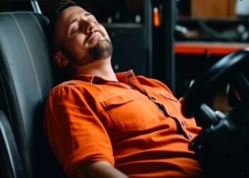 Caminhoneiro de roupa laranja repousando no banco do caminhão com expressão relaxada