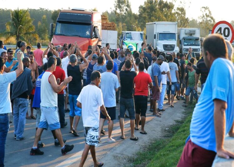 Grupo de caminhoneiros discute em frente a caminhões parados em estrada com placa de 40 km/h