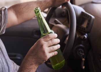 Motorista segurando garrafa verde ao dirigir veículo com uma mão no volante